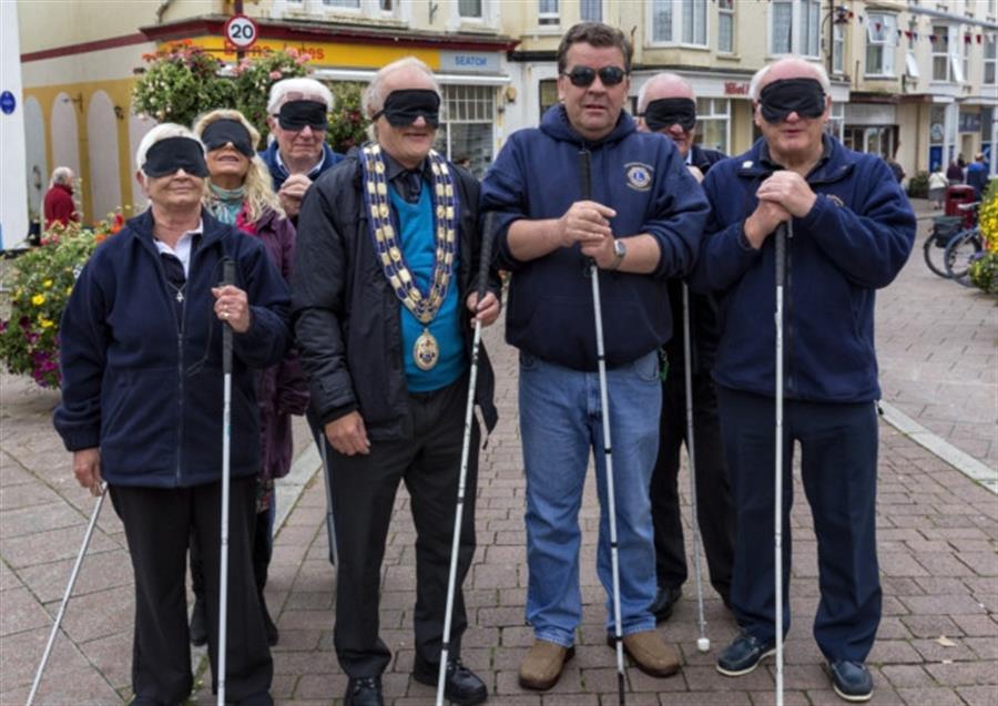 Consumers with white canes and blind folds look to camera and smile.